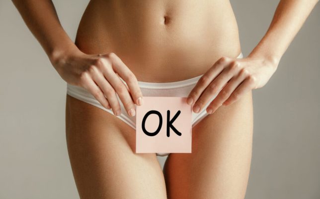 Woman health. Female model holding card near stomach. Young adult girl with paper with OK sign or symbol isolated on gray studio background. Cut out part of body. Medical problem and solution.